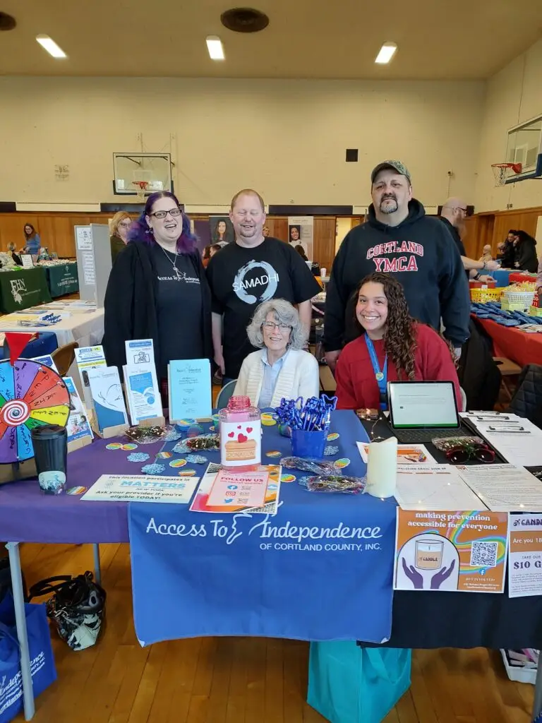 Five members of the CANDLE team smiling at the camera from behind a table displaying Access To Independence and CANDLE materials.