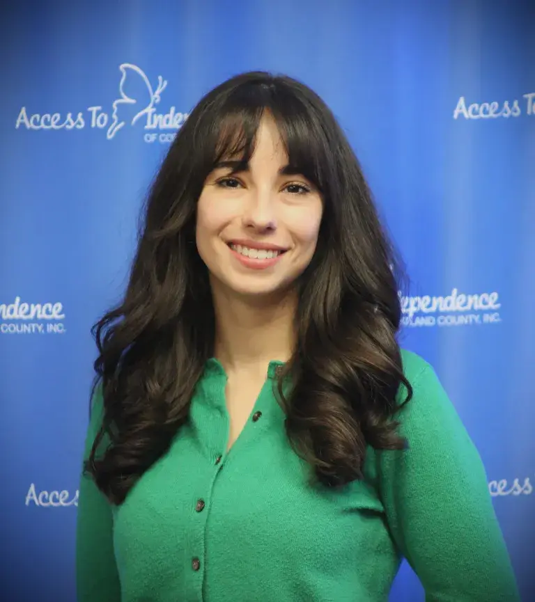 Stefania Buta, smiling, in a green cardigan in front of an Access To Independence backdrop.