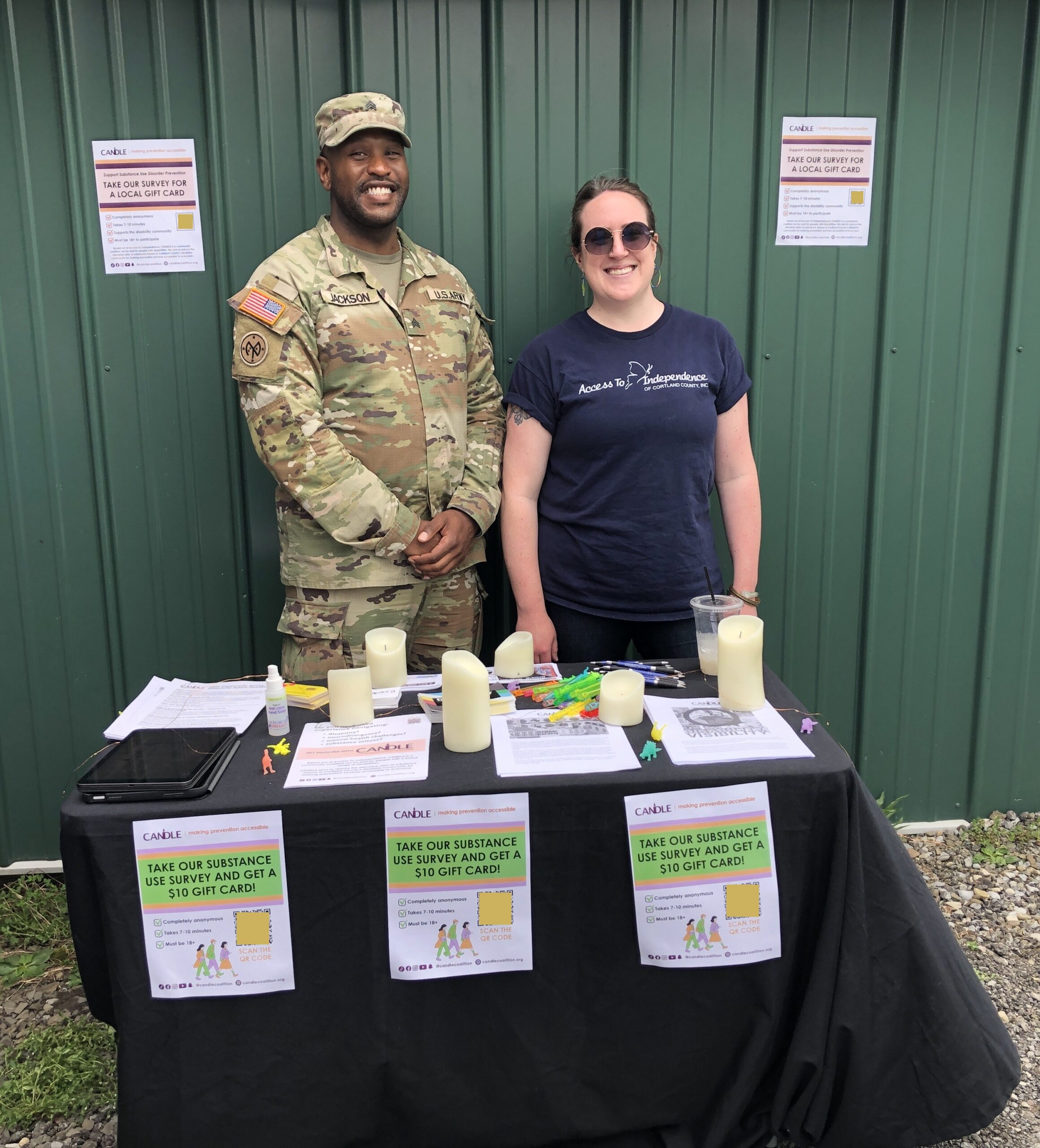 A black man in army uniform is standing with a white woman who is wearing sunglasses and an Access to Independence shirt