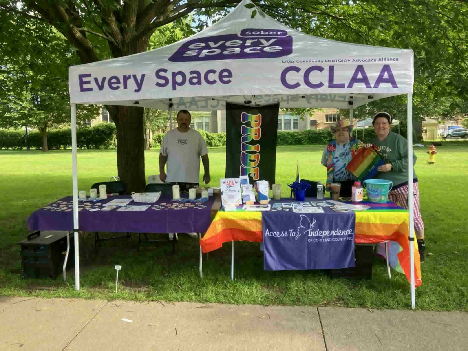 Three people stand behind the ATI and CANDLE table with pride flags decorating the booth.